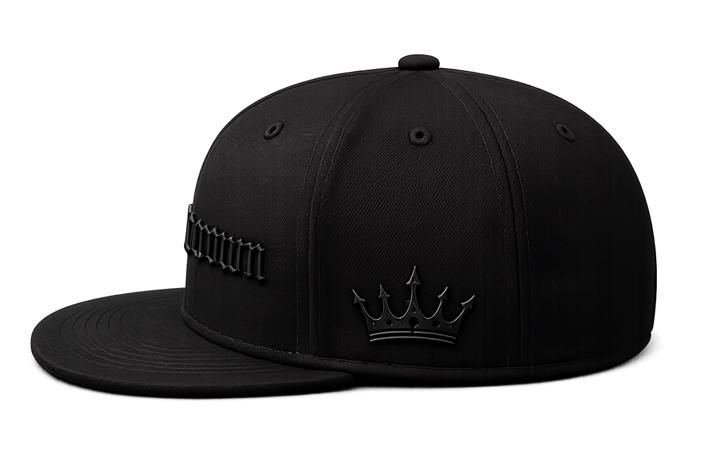 A black structured baseball cap with a flat brim, featuring a tonal black crown design with a crown emblem on the front and stylized text on the side, photographed on a solid white background.
